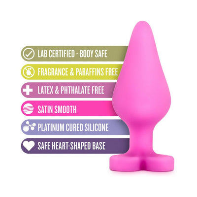 Pink silicone anal plug with heart-shaped base and text highlighting body safe, fragrance free, latex free, satin smooth, and platinum cured features.