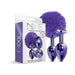 Nixie metal butt plug set with purple pom pom tail and jewel-inlaid metallic finish, shown with packaging box.