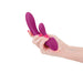 Hand holding a dark pink silicone dual-stimulation vibrator with a smooth, curved design and flexible arm.