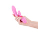 Hand holding a pink silicone dual-stimulation vibrator with smooth curves and ergonomic design.