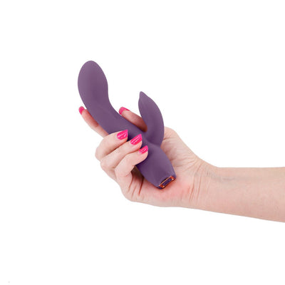Hand holding a dark purple silicone dual-stimulation vibrator with a smooth, curved design and rose gold accent.