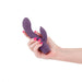 Hand holding a dark purple silicone dual-stimulation vibrator with a smooth, curved design and rose gold accent.