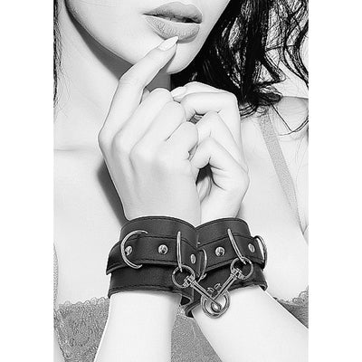 Black and white bonded leather wrist cuffs with metal D-ring connectors shown on model's wrists.