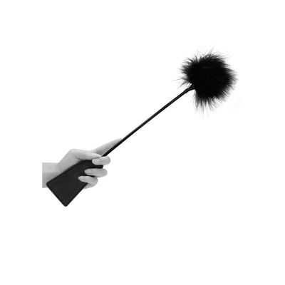 Hand holding a black leather crop with a soft black feather tickler tip on a white background.