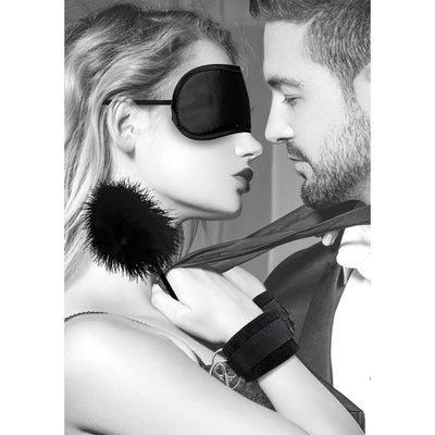 Couple engaging in intimate play with black satin blindfold, feather tickler, and velvet wrist cuffs from bondage kit.