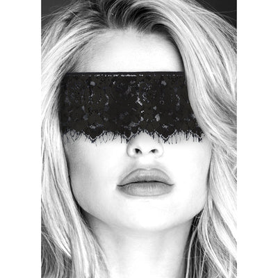 Close-up of a woman wearing a black lace eye mask with elastic straps covering her eyes.