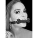 Black and white photo of a woman wearing a black silicone bone-shaped gag with adjustable bonded leather straps.