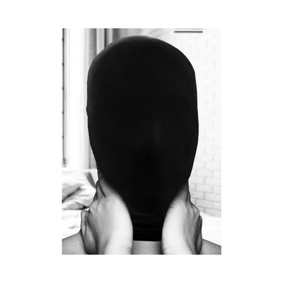 Black full-head spandex subjugation mask covering face, held gently by hands at the neck.