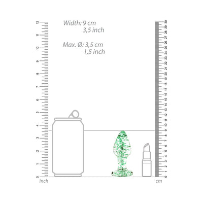 Clear glass butt plug with green speckles shown next to a soda can and lipstick for size comparison with rulers in inches and centimeters.