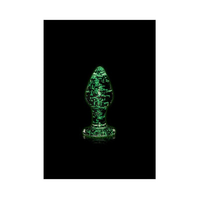 Clear glass butt plug glowing green in the dark with speckled design on a black background.