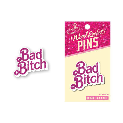 Pink glitter "Bad Bitch" enamel pin with bold script font, shown loose and on Wood Rocket branded backing card.