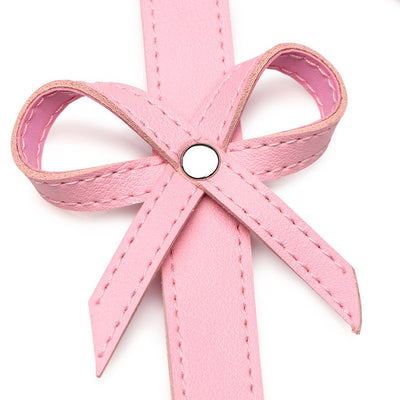 Close-up of a pink faux leather bow detail with stitched edges and a silver rivet center on a bondage harness strap.