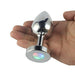 Hand holding a small, polished metal anal plug with a light-up LED base showing red, green, and blue colors.