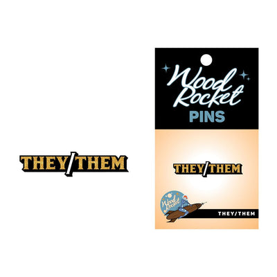 They/Them pronoun enamel lapel pin with gold glitter lettering on black backing card by Wood Rocket.