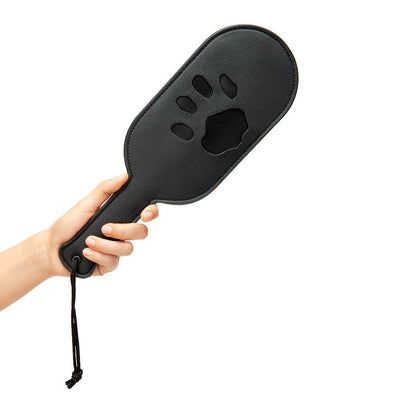 Hand holding a black paddle with a paw print imprint and a wrist strap on a white background.