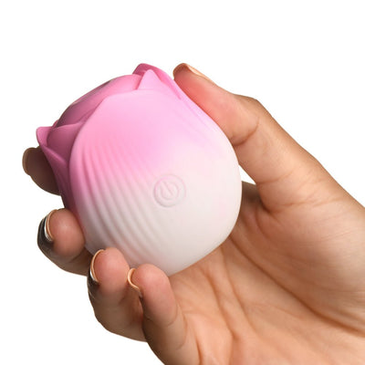 Hand holding a small pink and white rose-shaped silicone stimulator with a power button on the front.