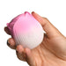 Hand holding a small pink and white rose-shaped silicone stimulator with a power button on the front.
