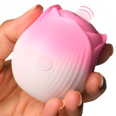 Hand holding a pink and white rose-shaped pulsing stimulator with a power button on the front and vibration waves shown.