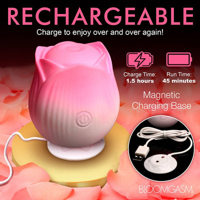 Pink rose-shaped pulsing stimulator on magnetic charging base with USB cable, surrounded by rose petals.