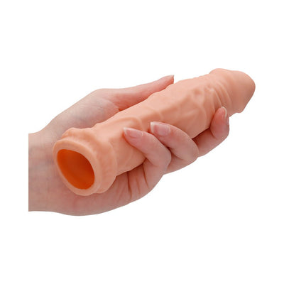 Hand holding a 7-inch vanilla-colored realistic penis extender sleeve with textured surface and open base.