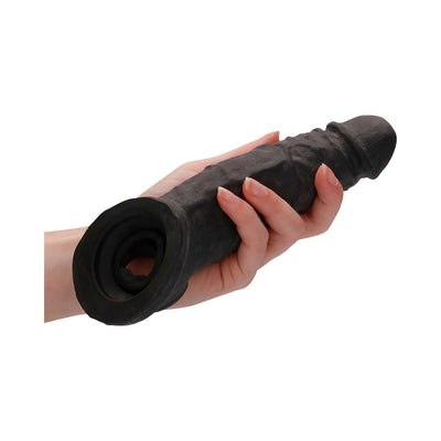 Hand holding a black 9-inch realistic textured penis extender with attached rings.