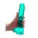 Hand holding a turquoise crystal clear realistic dildo with balls and suction cup base against a white background.
