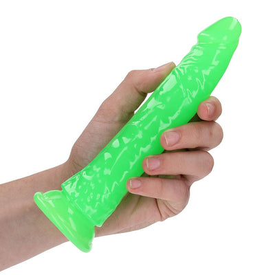 Hand holding a neon green glow-in-the-dark slim dildo with suction base on white background.