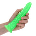 Hand holding a neon green glow-in-the-dark slim dildo with suction base on white background.