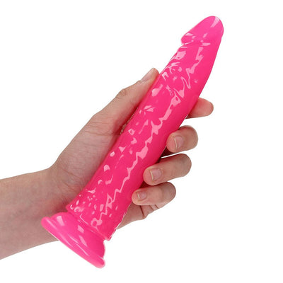 Hand holding a slim, bright pink glow-in-the-dark dildo with suction cup base against a white background.