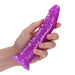 Hand holding a slim, purple glow-in-the-dark dildo with suction cup base against a white background.