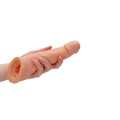 Hand holding a flesh-toned 8-inch realistic textured penis sleeve with open base on white background.