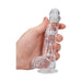 Hand holding a clear, realistic dildo with suction base and detailed texture.