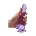 Hand holding a translucent purple realistic dildo with suction base and detailed texture.