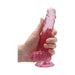 Hand holding a 7-inch pink realistic dildo with balls and suction cup base against white background.