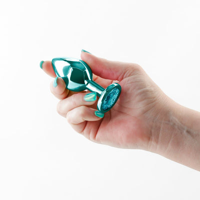 Hand holding a medium-sized teal chrome-plated metal anal plug with a jeweled base.