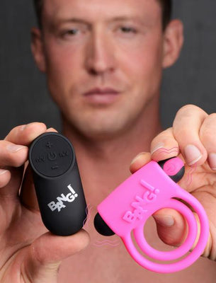 Man holding a pink vibrating silicone cock ring and black remote control from Bang! with logo visible.