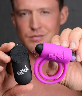 Man holding a pink vibrating cock ring with dual rings and a black remote control, both branded Bang!