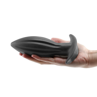 Hand holding a large black silicone Renegade Bomba anal plug with a flared base and textured design.