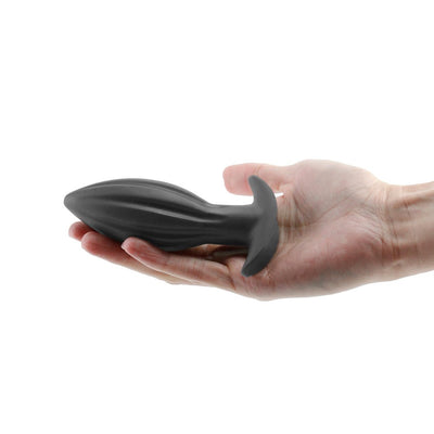 Hand holding a black silicone Renegade Bomba anal plug with a flared base and textured design.