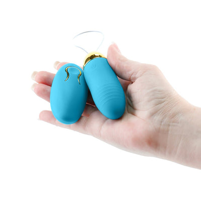 Hand holding a blue Revel Winx insertable remote bullet and matching wireless remote with gold accents.