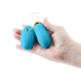 Hand holding a blue Revel Winx insertable remote bullet and matching wireless remote with gold accents.