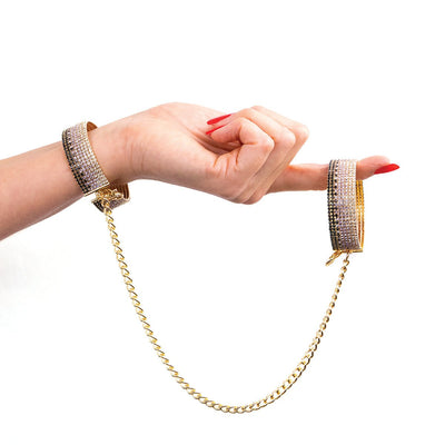 Hand wearing Rianne S Diamond Liz sparkling gold handcuffs with black, white, and purple stones connected by a gold chain.