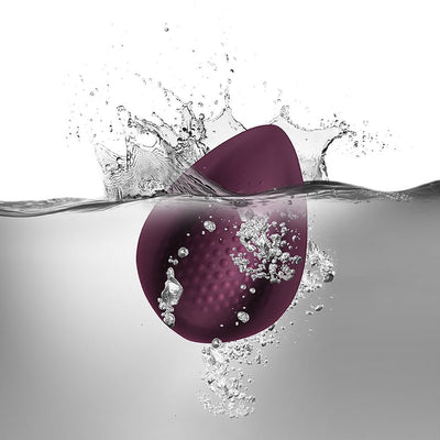 Burgundy waterproof silicone personal massager with textured surface submerged in water with splash effect.