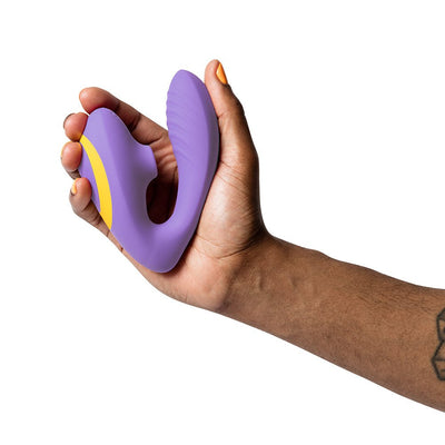 Hand holding a purple ROMP Reverb dual stimulator with yellow accent, designed for G-spot and clitoral stimulation.