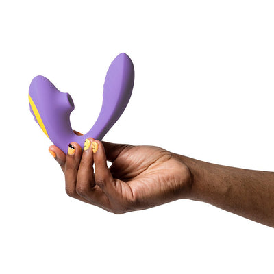Hand holding a purple ROMP Reverb dual stimulator with curved internal and external arms against a white background.