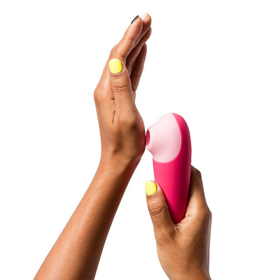 Hand holding Romp Shine X Pink silicone clitoral stimulator with yellow nail polish on white background