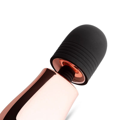 Close-up of a compact rosy gold mini massager with a soft black silicone head on a white background.