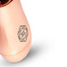 Close-up of the rosy gold mini massager with geometric logo on a smooth metallic surface against a white background.