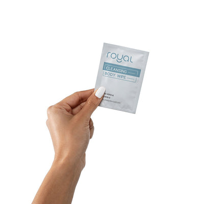 Hand holding a single Royal Condom Intimacy Cleansing Body Wipe packet with white and blue packaging.