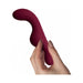 Hand holding a compact, curved maroon Ruby Glow Rosa Saddle Vibrator with smooth silicone finish.